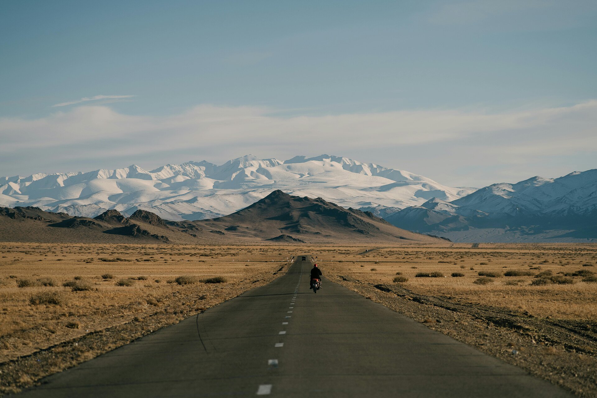 Ein Motorrad fährt auf einer Straße gen Horizont - endlose Weite und Gebirge in der Ferne der Mogolei