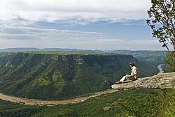Ein Wanderer legt eine Pause ein und blickt in die satt-grüne Landschaften der Drakensberge im Royal Natal Nationalpark